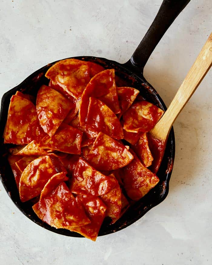 Tortilla chips being gently folded and simmered in a tomato and chipotle sauce.