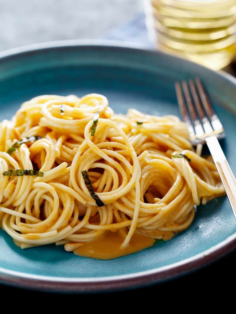 A close up of uni spaghetti on a turquoise plate with a fork.