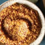 Homemade whole grain mustard in a bowl with a spoon next to it.