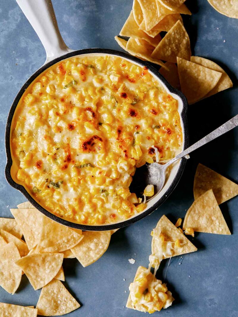 A pan of Korean corn cheese with a spoon and tortilla chips.