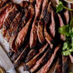 Carne Asada on a cutting board with limes and cilantro on the side.