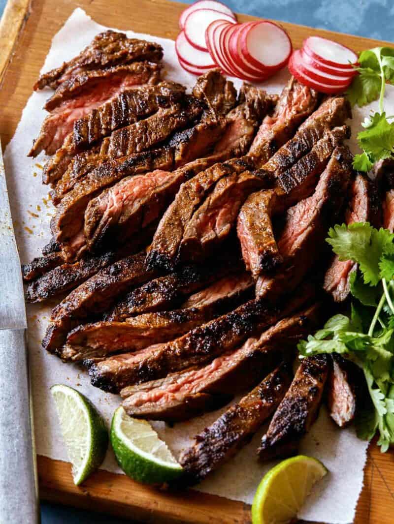 Carne Asada recipe cut up  on a cutting board with lime wedges and a knife. 