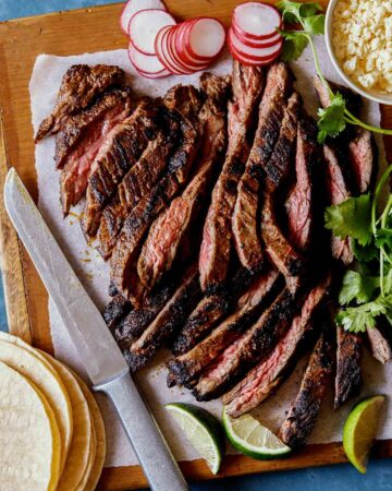 Sliced Carne Asada with tortillas, radishes, lime wedges, and a knife.
