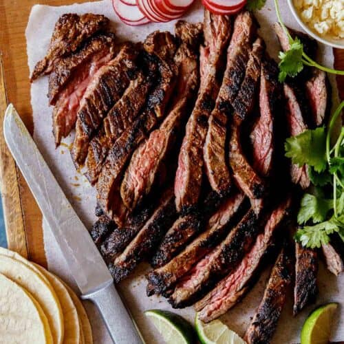 Sliced Carne Asada with tortillas, radishes, lime wedges, and a knife.