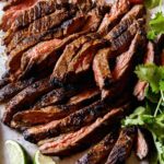 Carne Asada on a cutting board with limes and cilantro on the side.