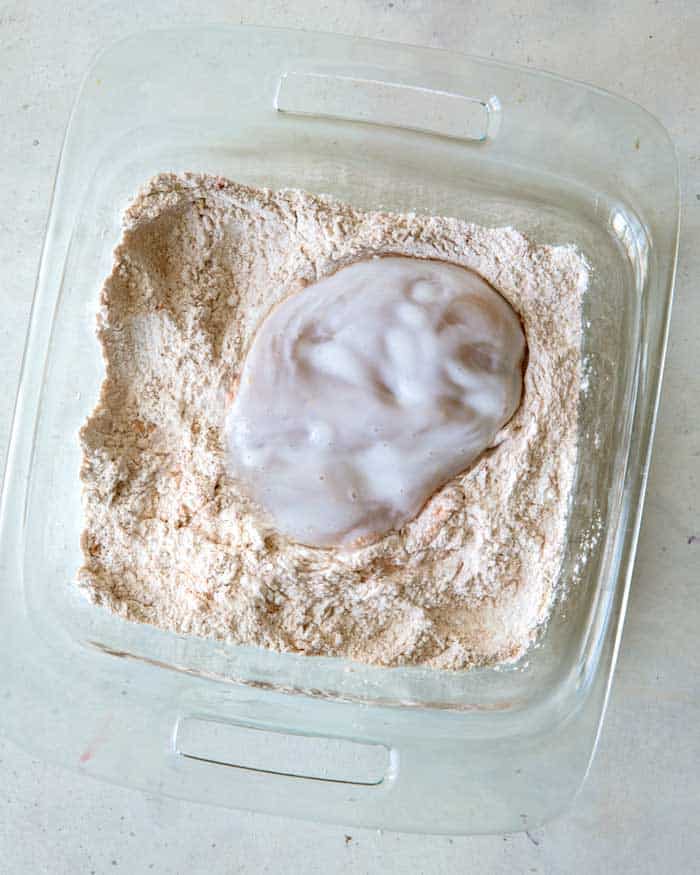 Chicken being tossed in a flour mixture to make a chicken sandwich.