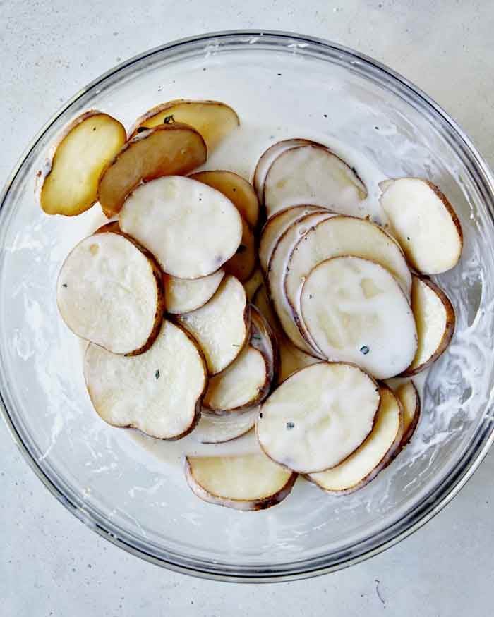 Potato slices soaking on a bowl on buttermilk with other spices. 
