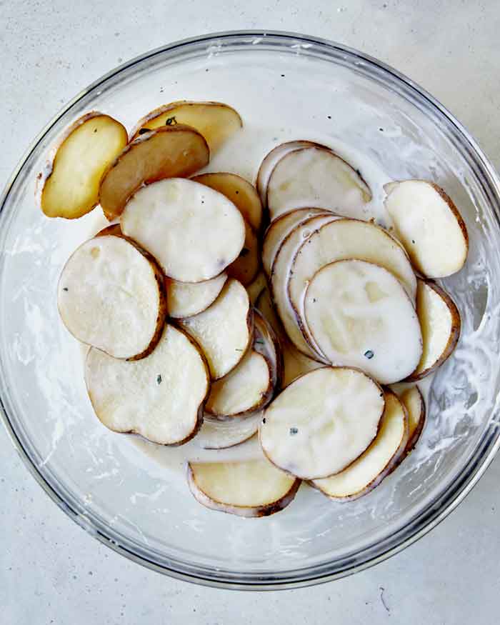 Potato slices soaking on a bowl on buttermilk with other spices.