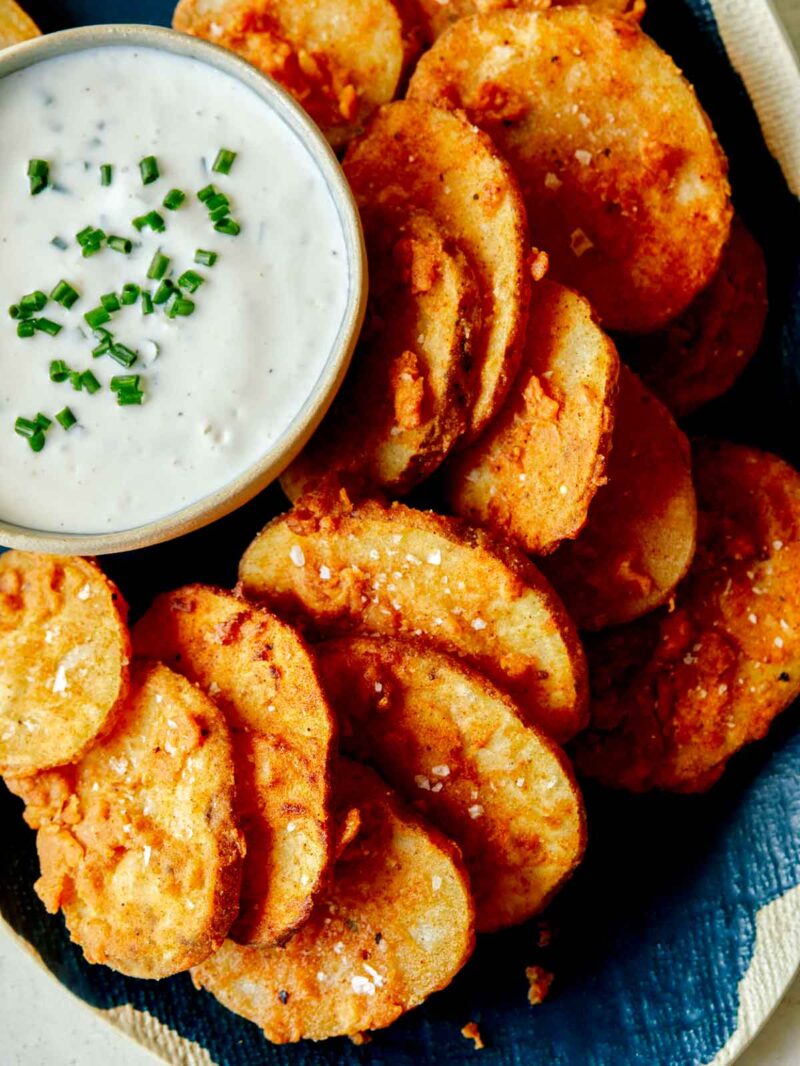 An overhead shot of chicken fried potato slices on a platter with a bowl of ranch dressing. 