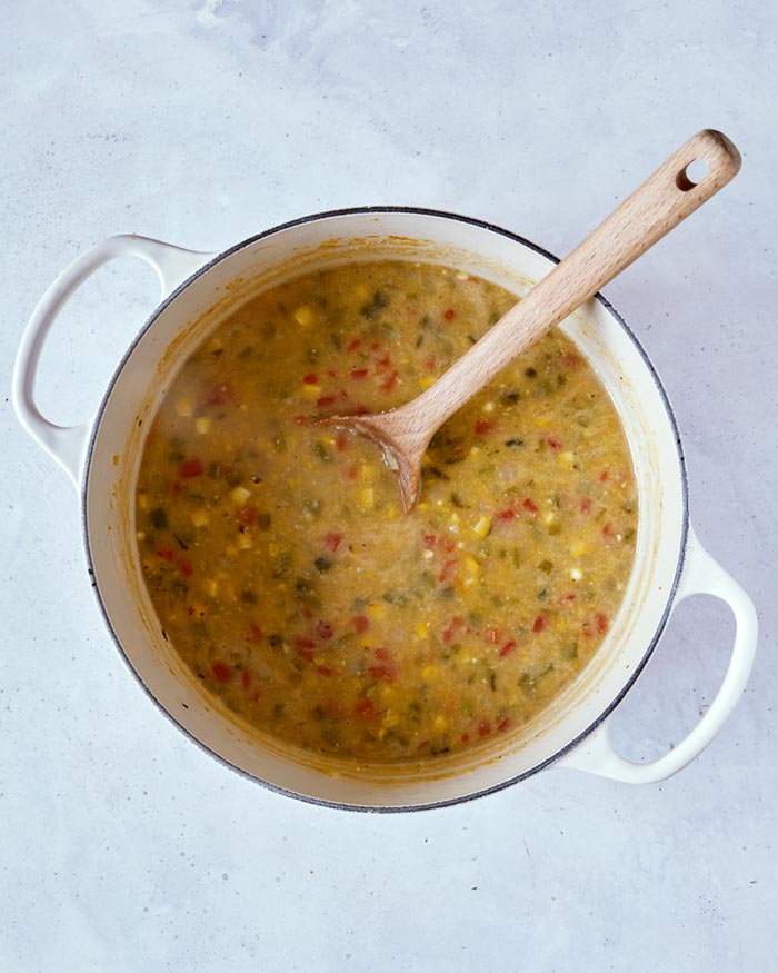 Tequila and the blended stock mixture in a pot overhead with a wooden spoon in it.
