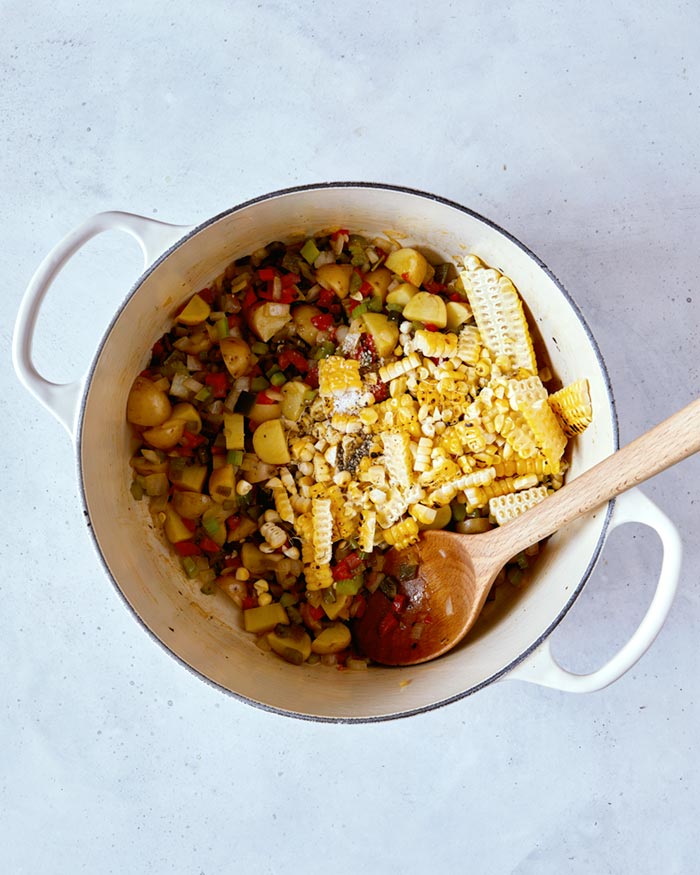 Corn kernels added to the soft vegetables in a stock pot.