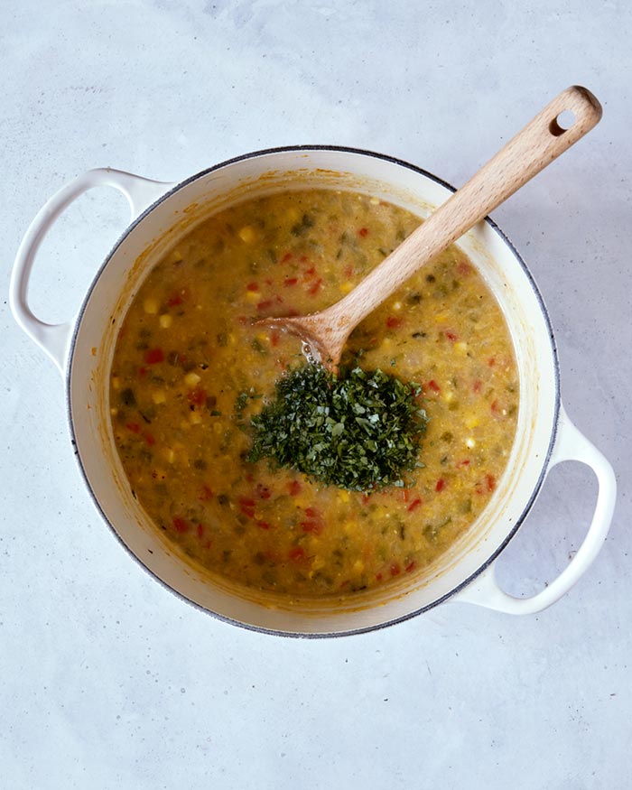 Herbs added to the stock pot with the soup mixture in it and a wooden spoon.