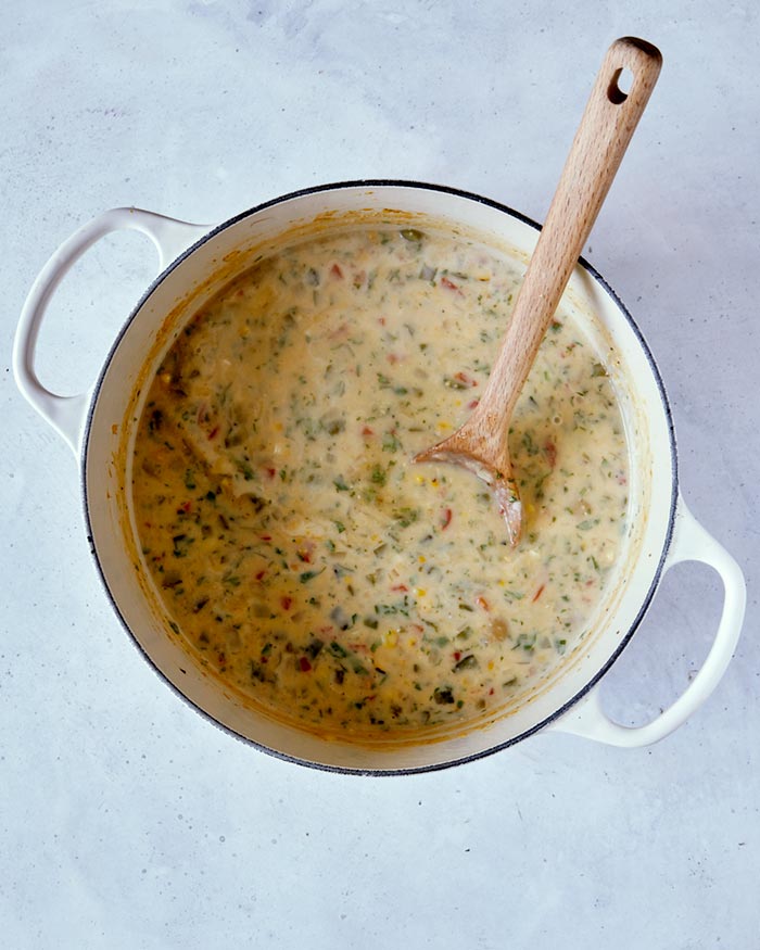 Cream added to the roasted corn mixture in a stock pot with a wooden spoon.