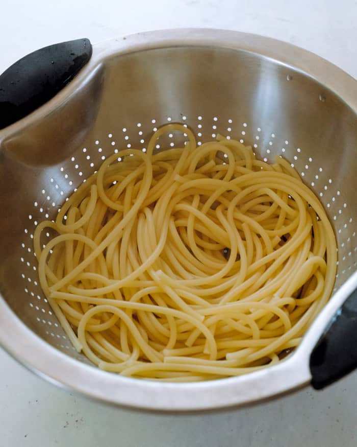 Cooked bucatini noodles in a strainer.