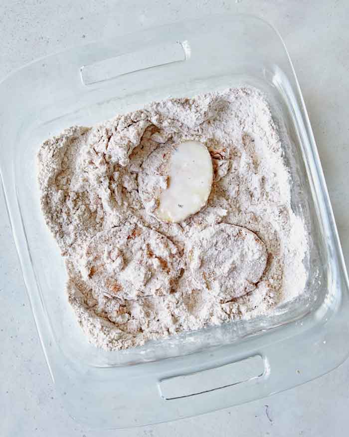 Potato slices being dredged in a shallow baking dish.