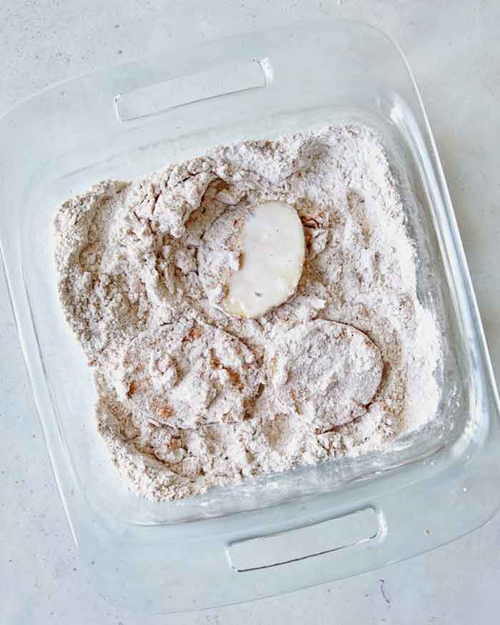 Potato slices being dredged in a shallow baking dish. 