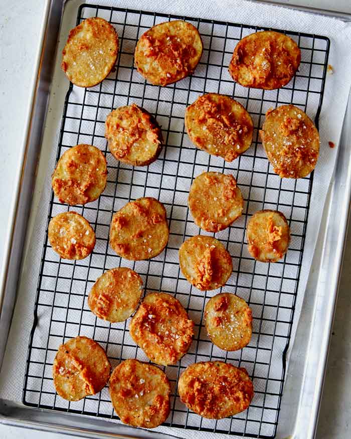 Freshly fried chicken fried potatoes on a cooling rack with salt on them.