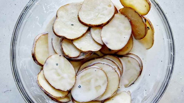 Thinly sliced potatoes in a bowl full of a buttermilk mixture.