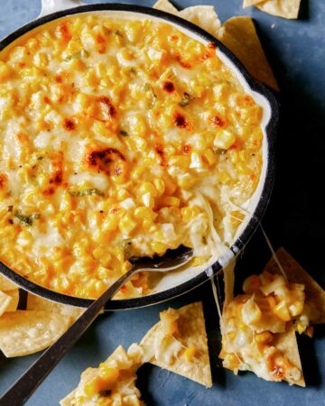 Korean cheese corn baked in a pan with spoon next to dipped chips and melted cheese, part of our Thanksgiving appetizers collection.
