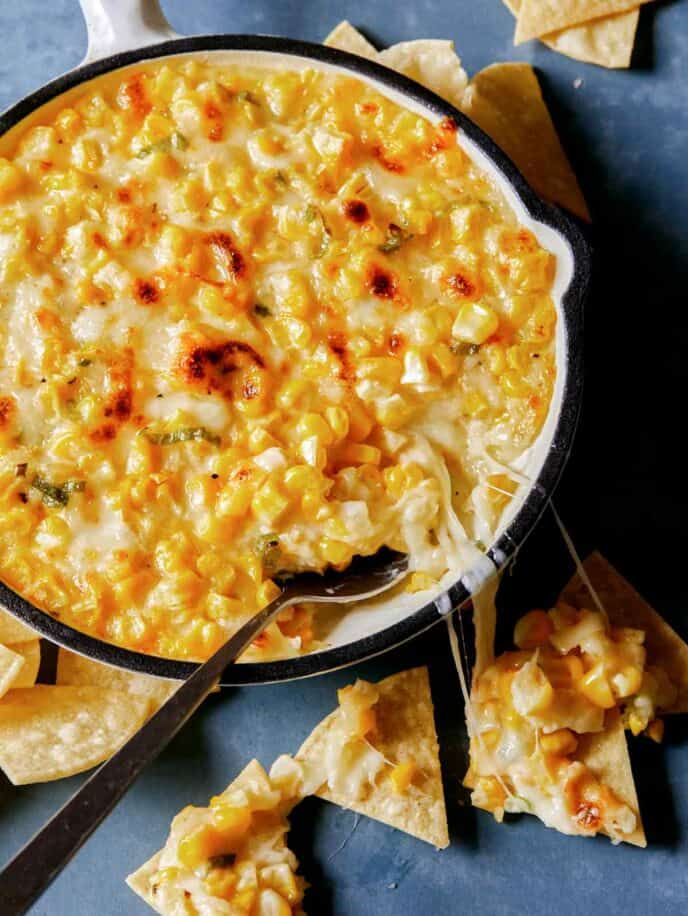 Korean cheese corn baked in a pan with spoon next to dipped chips and melted cheese, part of our Thanksgiving appetizers collection.