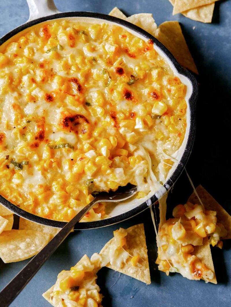 A pan of Korean corn cheese with a spoon and tortilla chips.