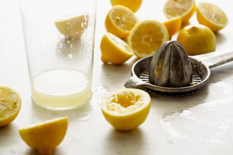 Lemons being freshly squeezed on a surface into a glass. 
