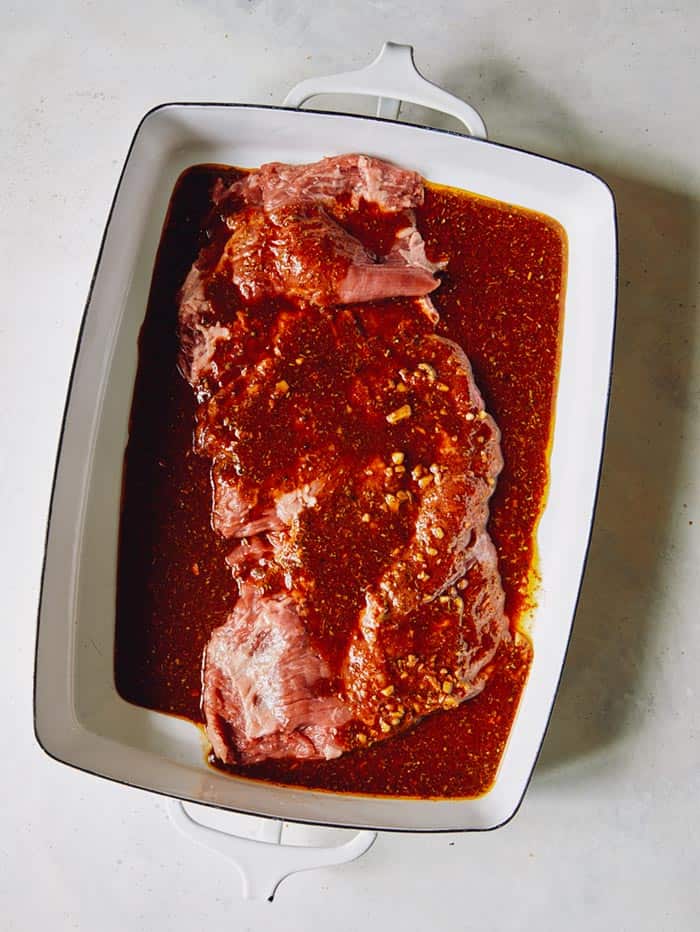 Skirt steak in a shallow baking dish with marinade poured all over it.