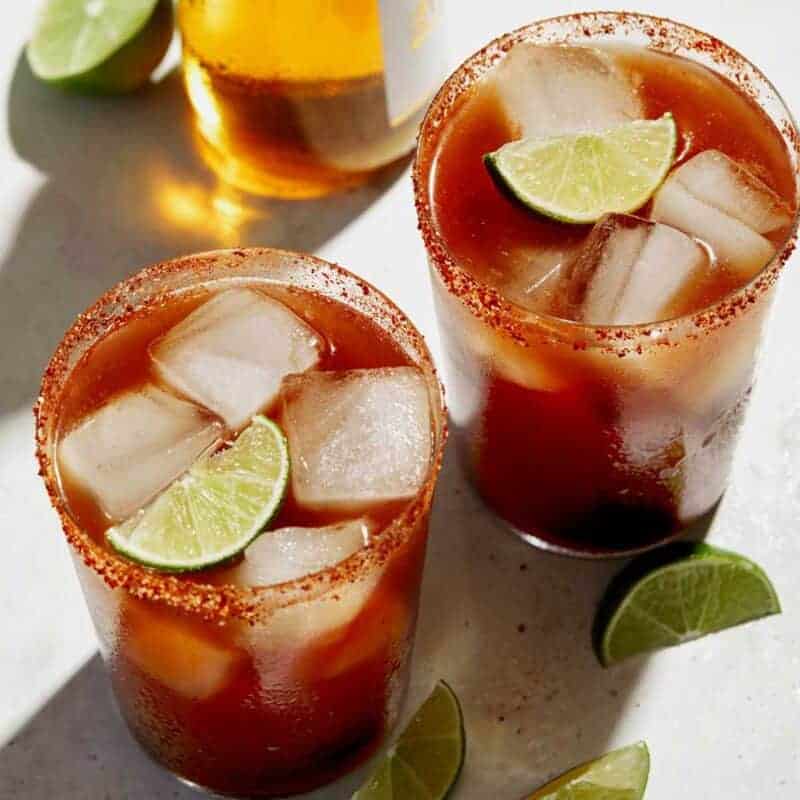 Beer bottle and glasses of Michelada with lime wedge garnish.