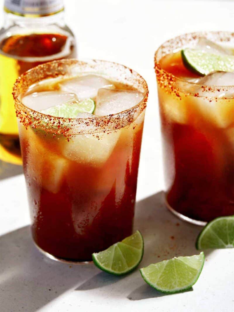 A close up of two glasses of Michelada with lime wedge garnish.