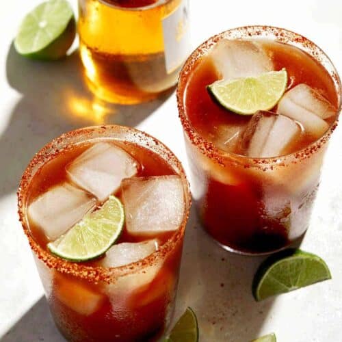 Beer bottle and glasses of Michelada with lime wedge garnish.