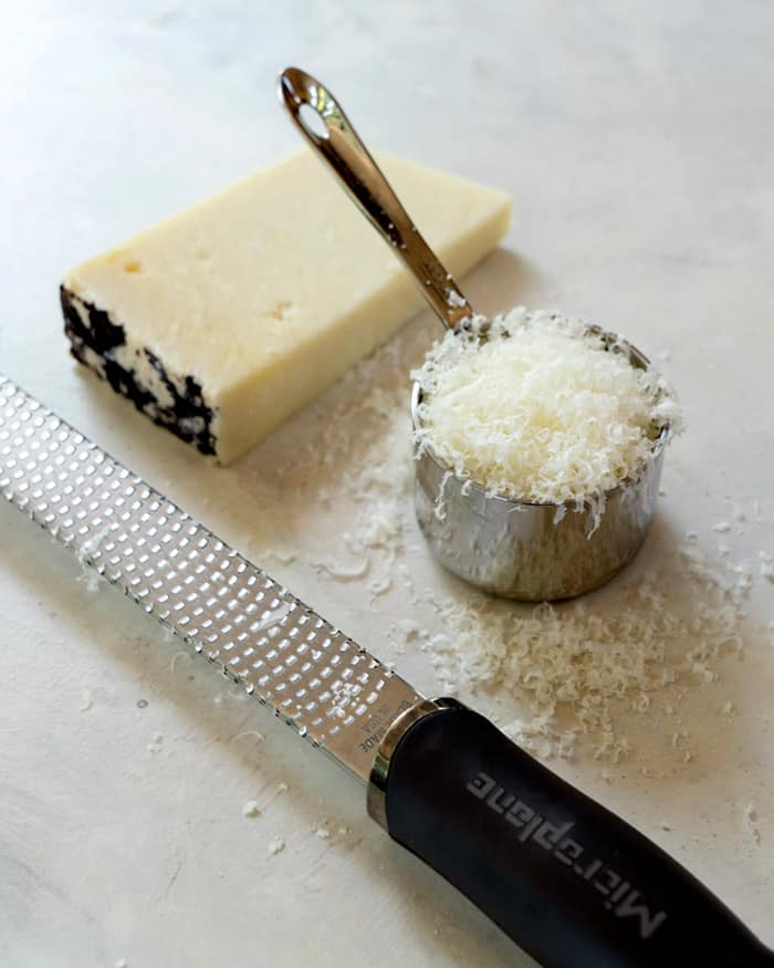 Block of cheese, cup of grated cheese, and a microplane. 