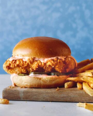 A close up of Popeyes Chicken Sandwich with fries on a wooden board.