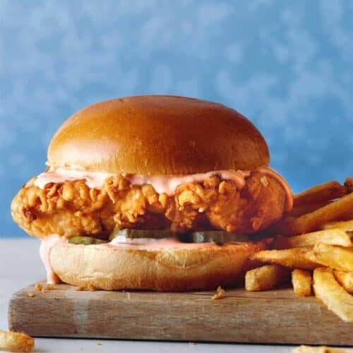 A close up of Popeyes Chicken Sandwich with fries on a wooden board.