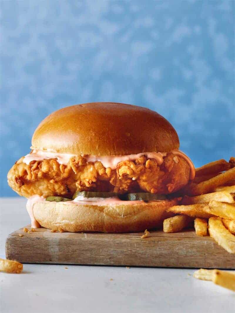 Popeyes chicken sandwich on a cutting board with french fries on the side. 