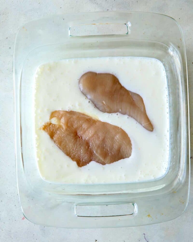 Chicken breasts in buttermilk in a glass dish.