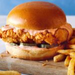 Popeyes chicken sandwiche on a cutting board with french fries next to it.