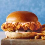 Close up on a popeyes chicken sandwich recipe with french fries next to it.