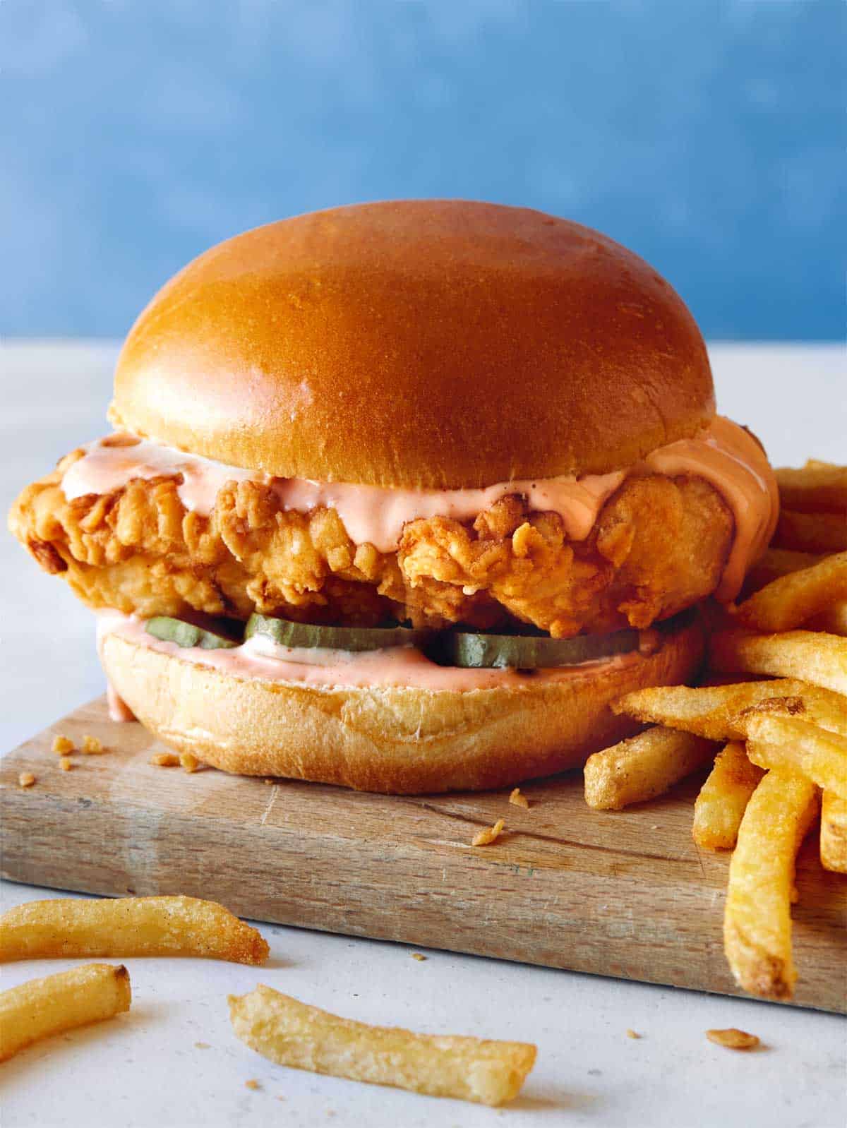 Popeyes fried chicken sandwich on a cutting board with french fries.