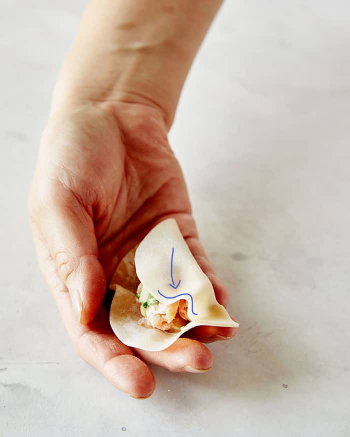 The process of folding the wonton wrapper to make a potsticker.