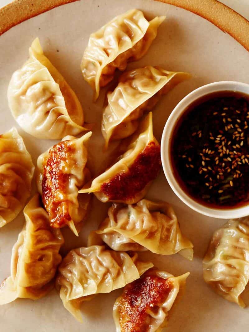 Potstickers on a plate next to a small bowl of potsticker sauce.