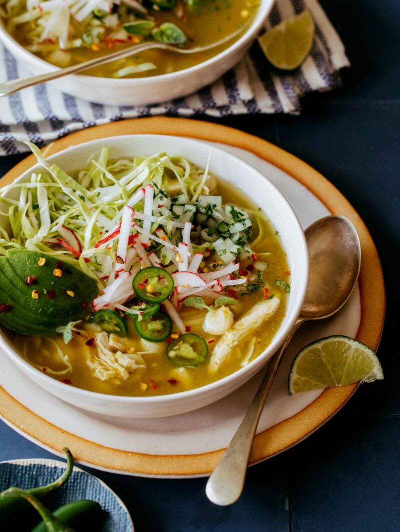 Pozole Verde de Pollo in two bowls with lime wedges on the side.