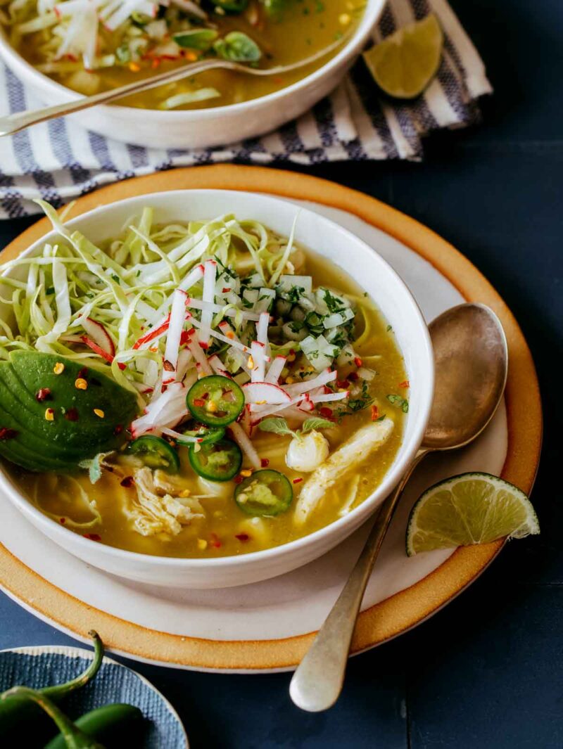 Pozole Verde de Pollo in two bowls with lime wedges on the side. 