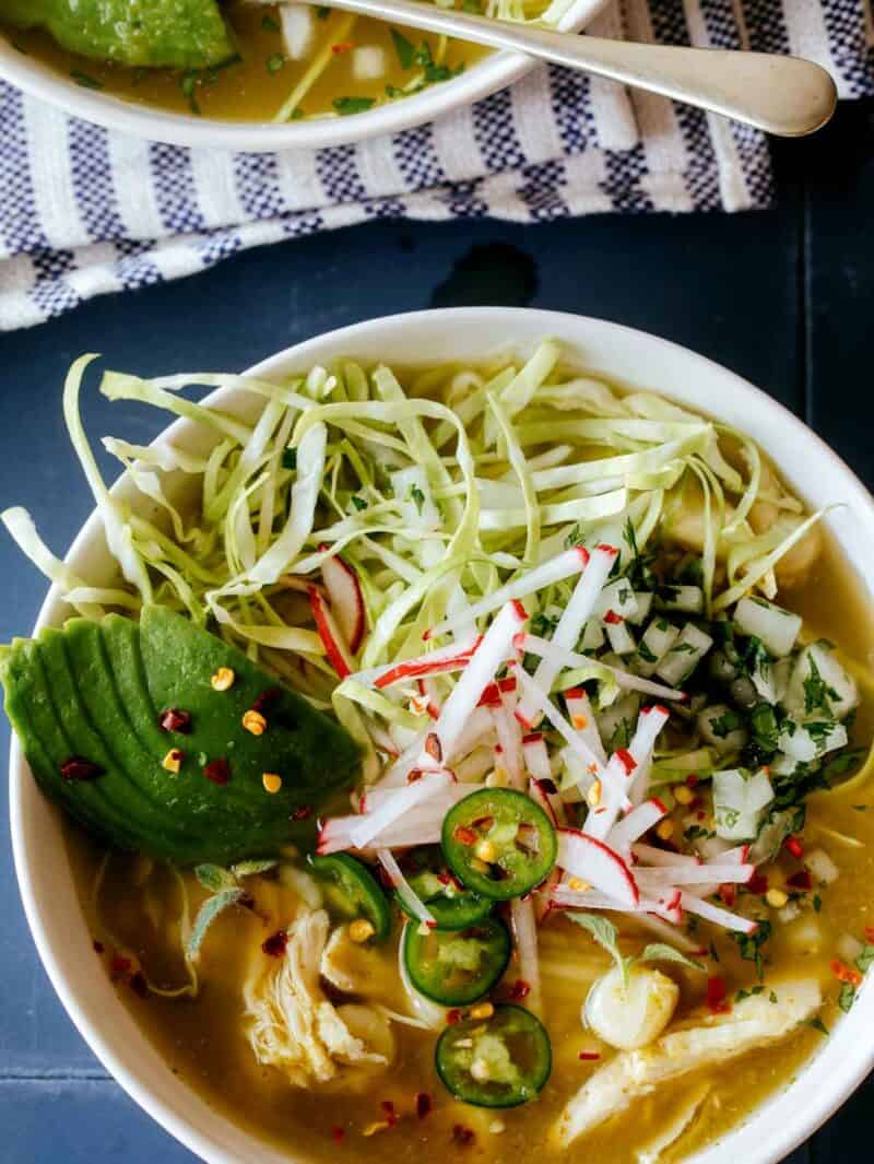 Pozole Verde De Pollo in a bowl with toppings and a spoon next to it. 