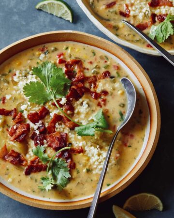 A bowl of corn chowder garnished with bacon and cilantro with a spoon.