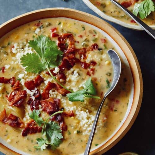 A bowl of corn chowder garnished with bacon and cilantro with a spoon.