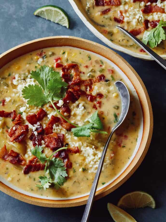 A bowl of corn chowder garnished with bacon and cilantro with a spoon.