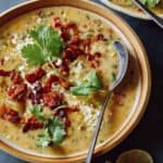 A bowl of corn chowder garnished with bacon and cilantro with a spoon.