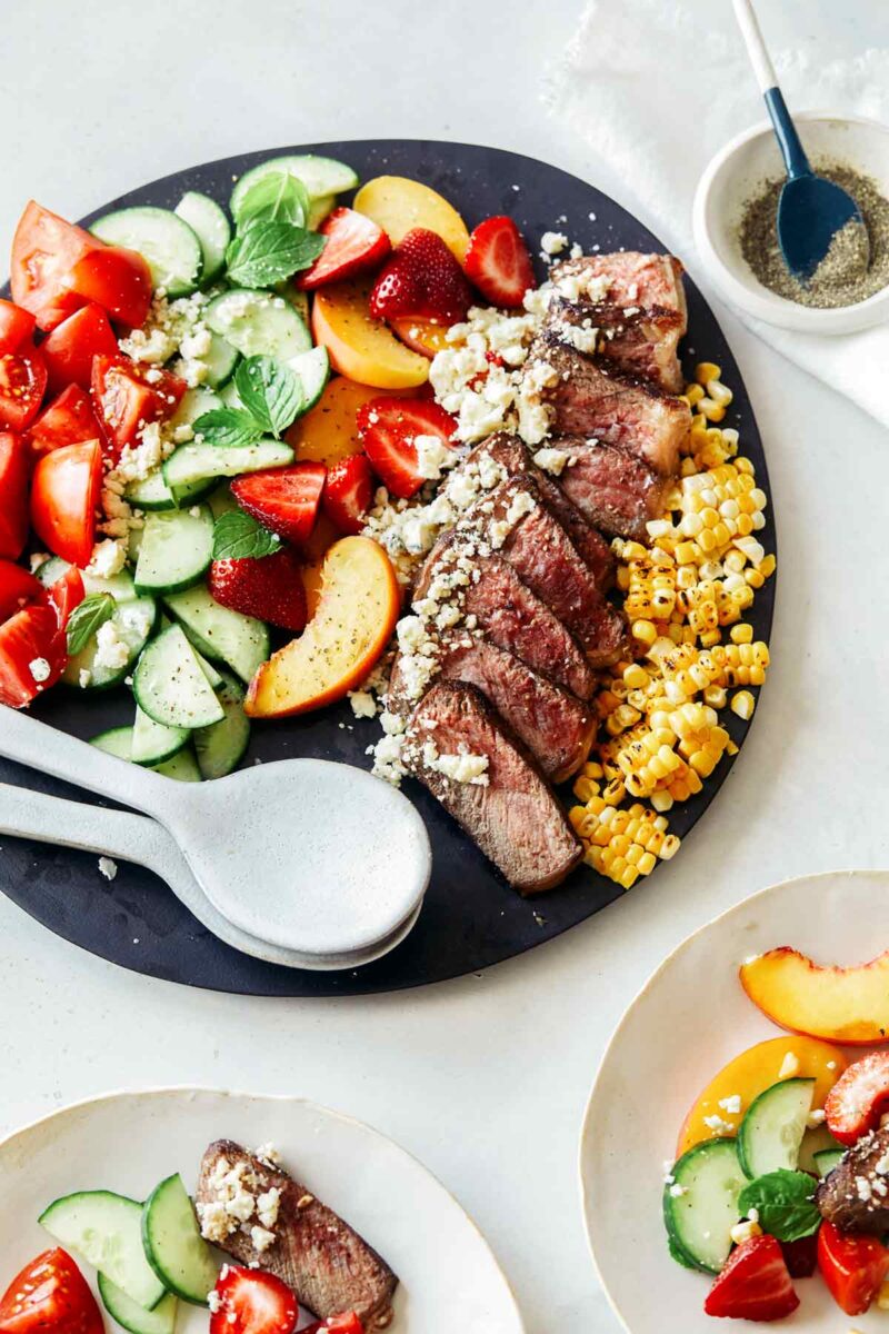 A steak salad on a platter with some served onto plates next to it. 