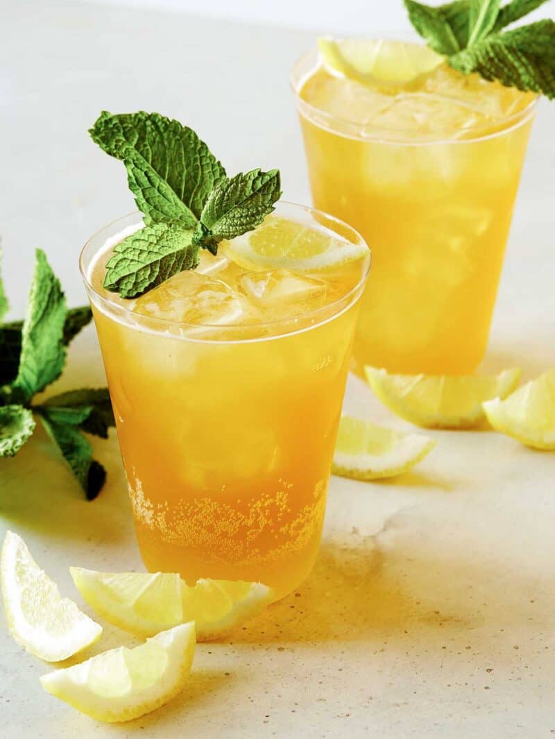 A summer shandy cocktail in glasses with ice, garnished with lemon wedges and mint leaves.