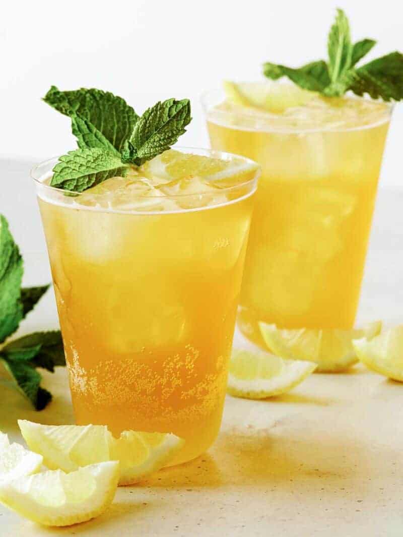 Summer Shandy cocktail on a surface with lemon wedges and mint. 